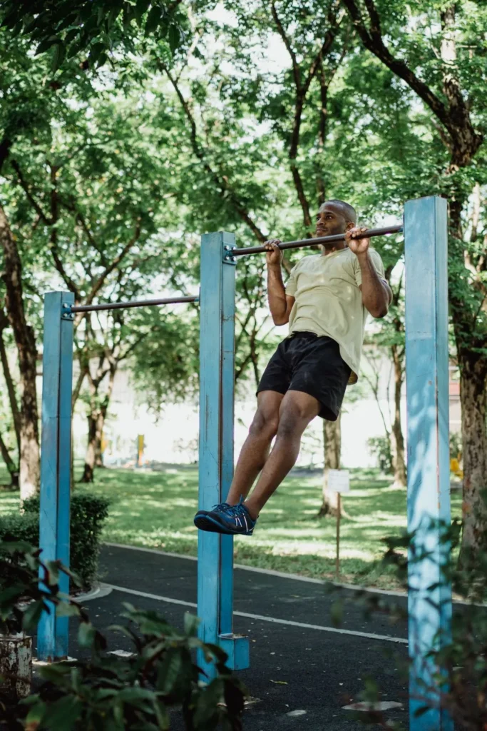 Homme noir avec réalisant des tractions à la barre fixe dans un park - position haute