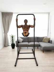 Homme noir réalisant un L-sit en suspension avec la barre de traction The Big bar de baseblocks dans un salon