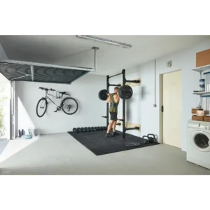 Homme avec barre de musculation et disques sur les épaules se préparant à faire des squat avec le rack mural de musculation pliable Corength decathlon dans son garage